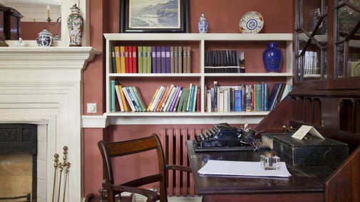 Large wooden desk with bookshelves and red walls behind it